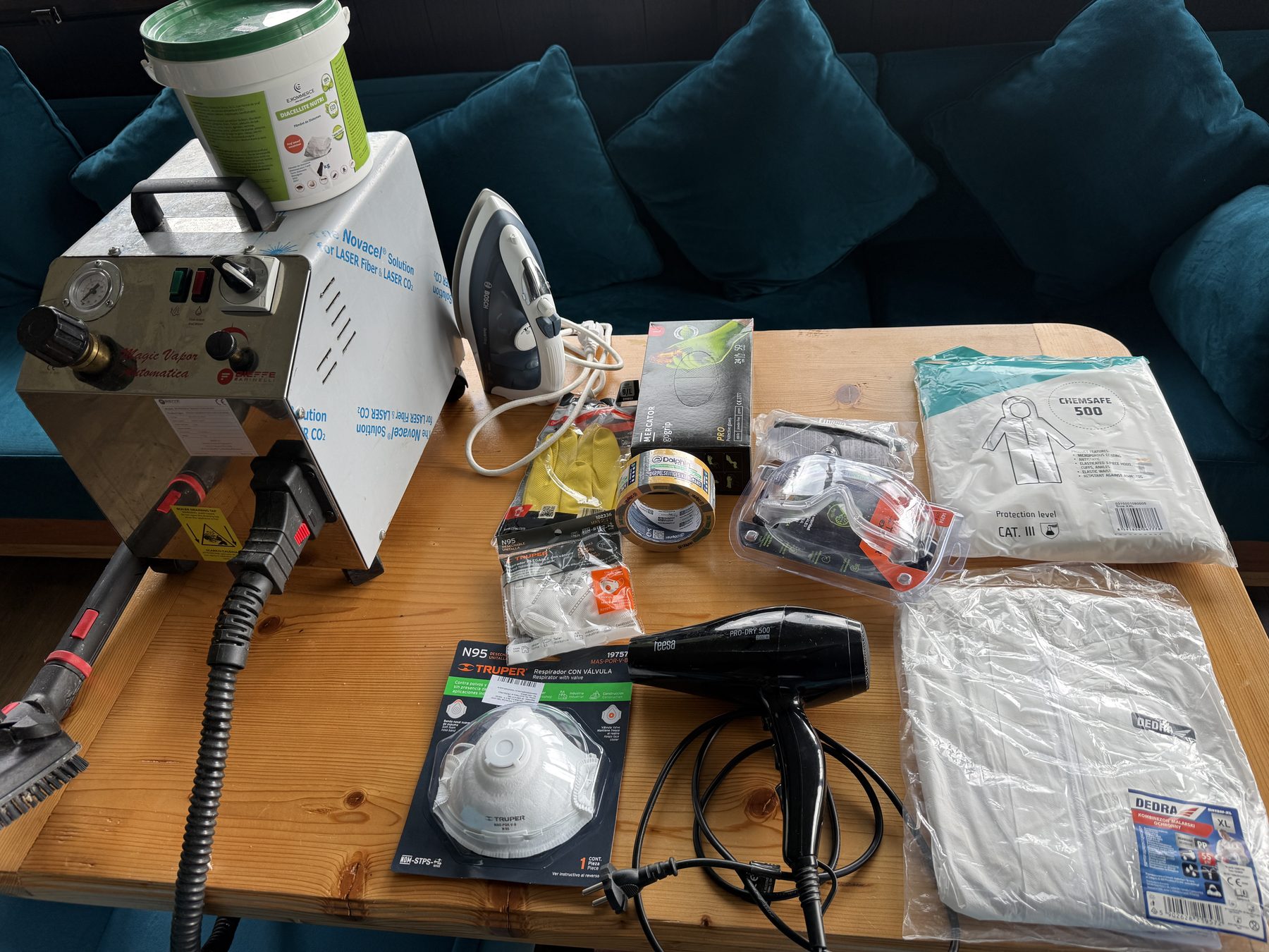 The actual bed bug treatment kit on a workbench: industrial steamer, diatomaceous earth, iron, N95 masks, nitrile gloves, goggles, hazmat suit and tape