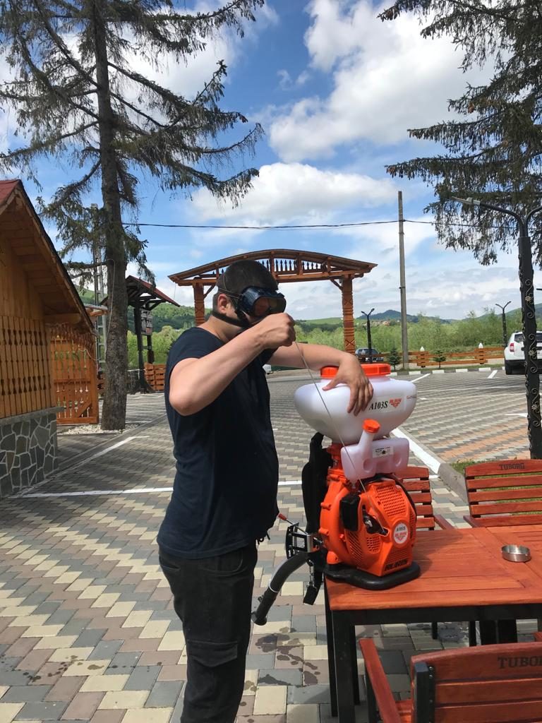 Norbi spraying the property with a backpack mist sprayer outside Hotel Casa Norbi
